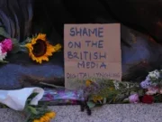 Flowers on the floor with sign written on cardboard saying 'Shame on the British media. Digital lynching'
