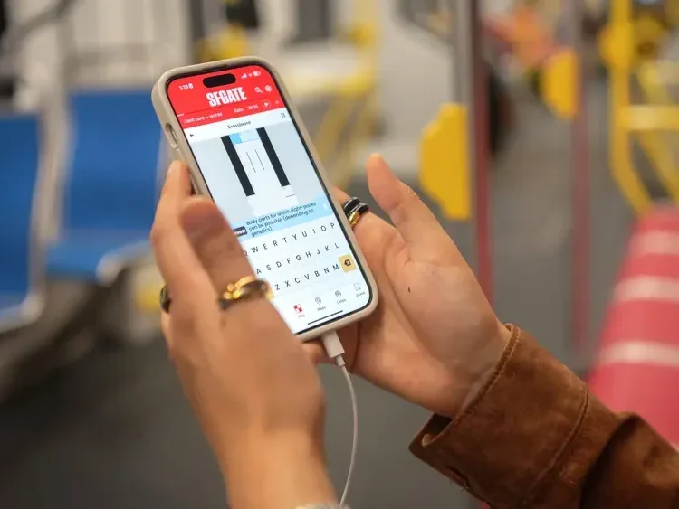 SFGate app showing on phone being held by woman's hands on subway train