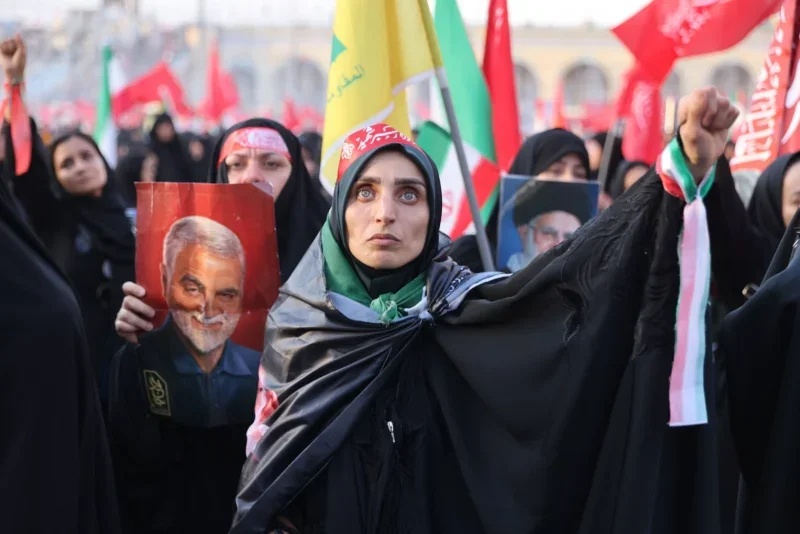 Woman clad in black and with a fist raised to the air in sea of mourners in Iran
